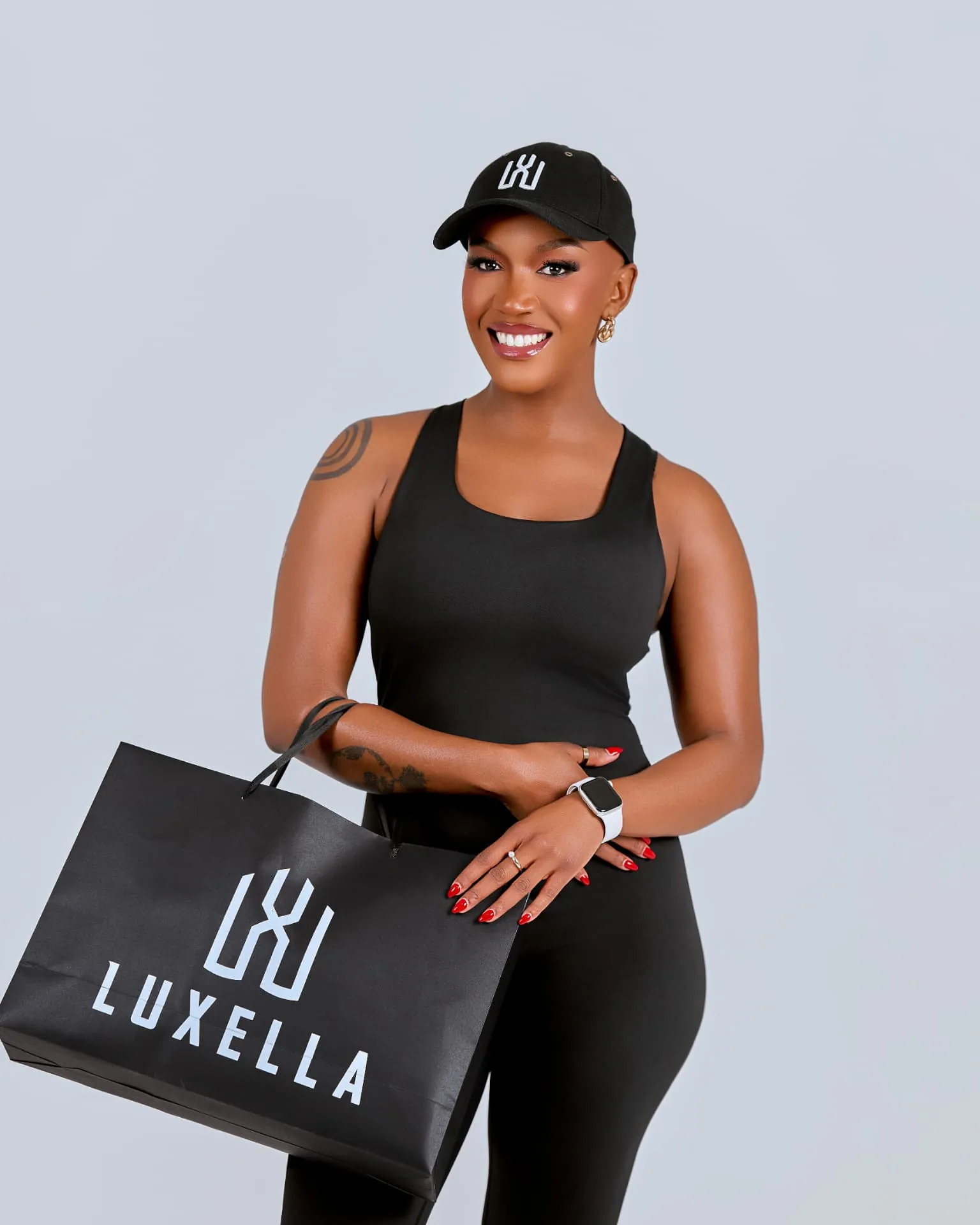 Model smiling in Luxella tank and cap holding a Luxella shopping bag