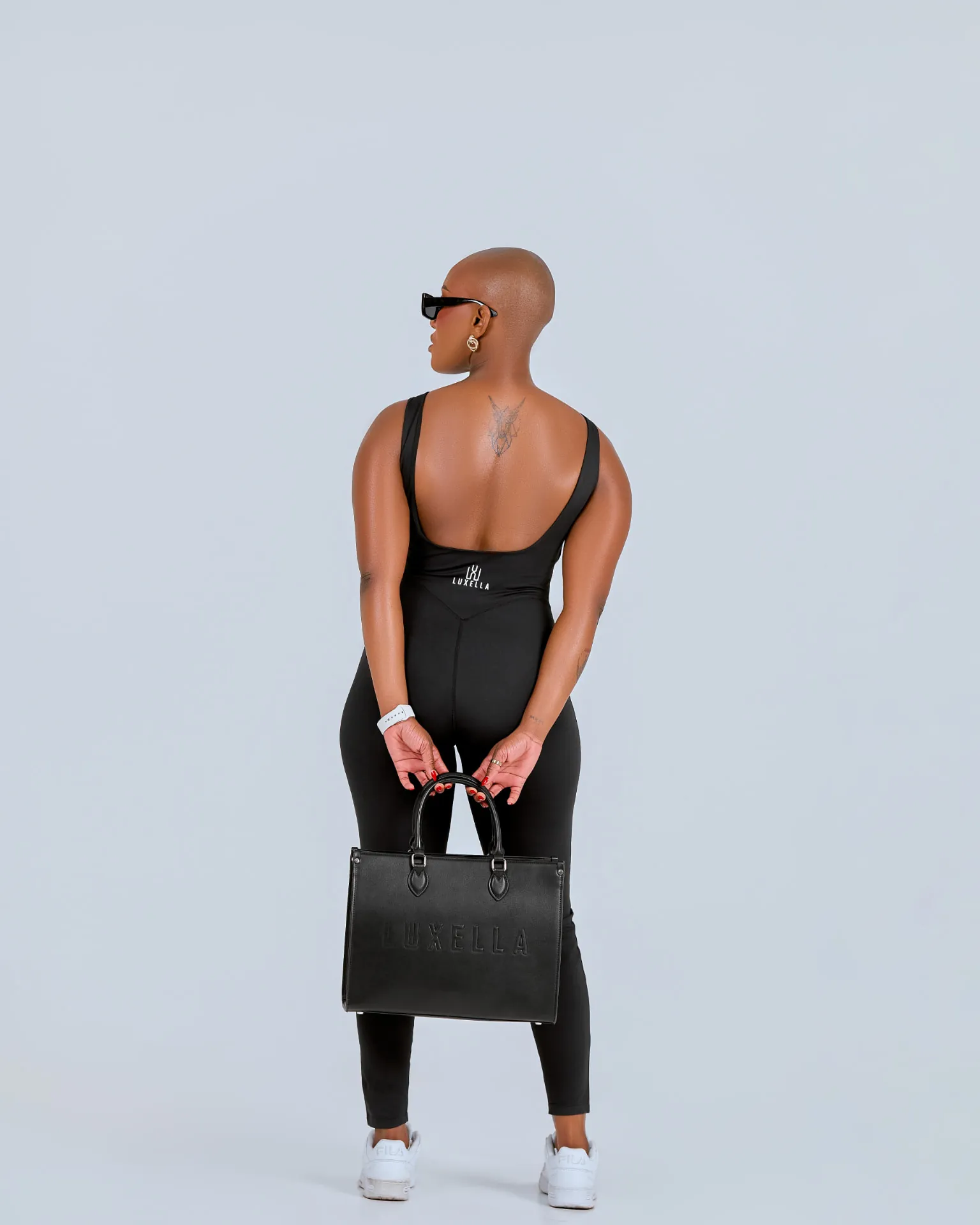 Model from behind in a black Luxella bodysuit holding the embossed Luxella shopper