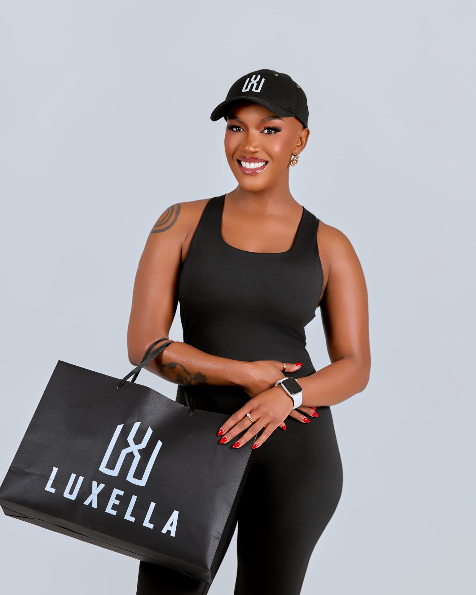 Model smiling in Luxella tank and cap holding a Luxella shopping bag